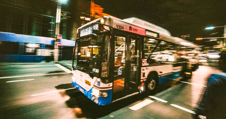 Ein typischer Bus aus dem regionalen Personenverkehr fährt auf einer mehrspurigen Straße. Bewegungsunschärfe im Motiv deutet auf eine zügige Geschwindigkeit des Fahrzeugs hin.